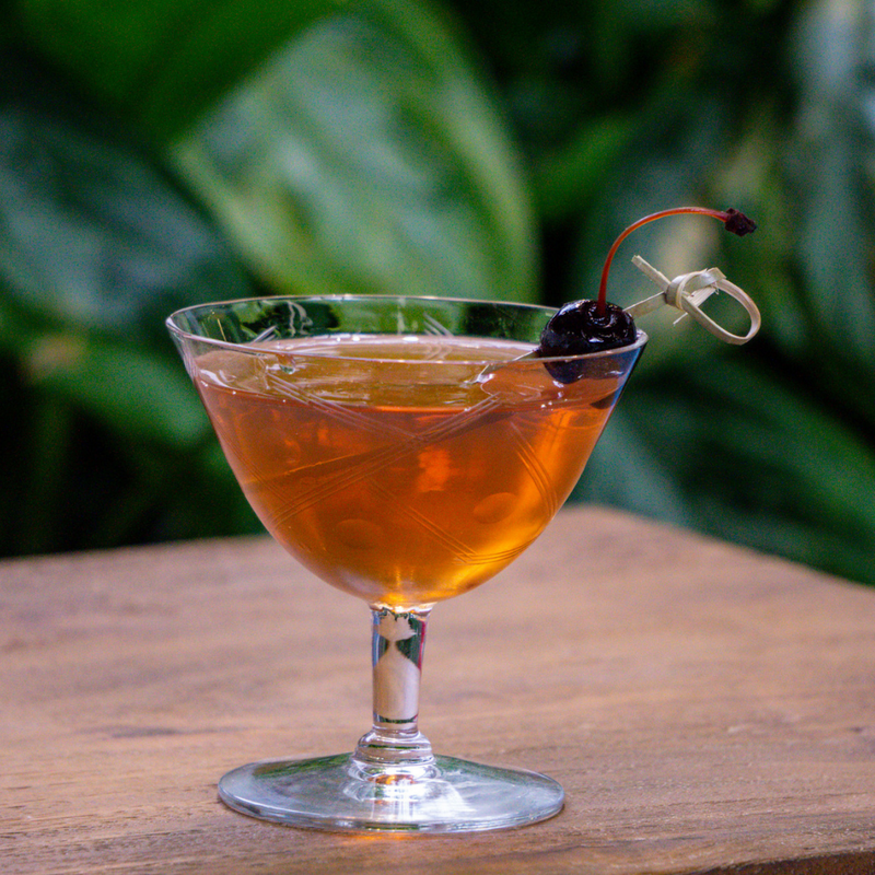 light brown bourbon cocktail in a saucer glass with a cherry garnished that has been skewered